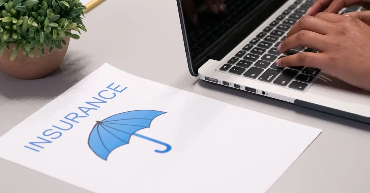 Gros plan sur des mains tapant sur un ordinateur portable avec un document d'assurance visible sur le bureau.