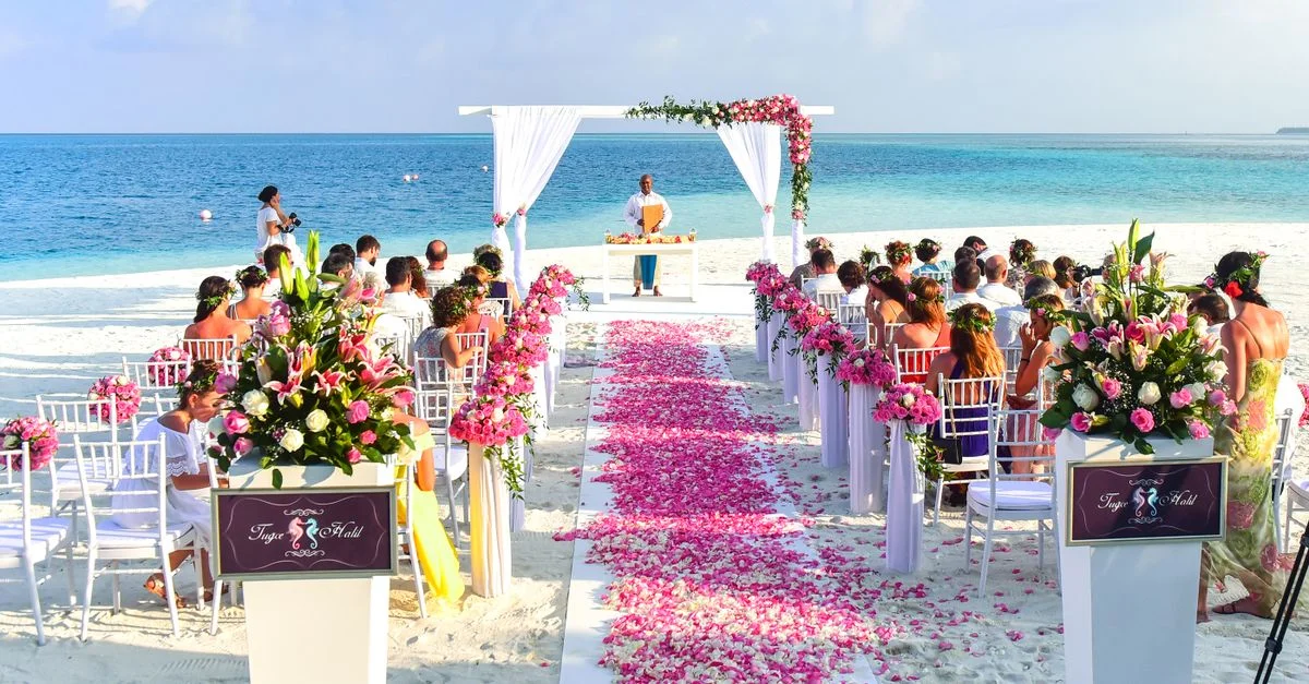 Un magnifique cadre de mariage en plein air sur la plage avec des pétales de rose, des invités et une vue sur l'océan.