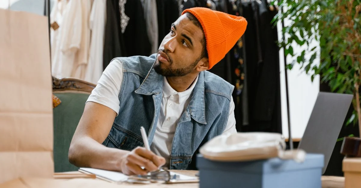 Homme en bonnet lumineux écrivant à une table dans une boutique de vêtements.